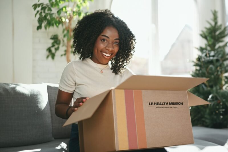 Mujer feliz recibiendo un paquete de productos LR Health & Beauty en casa.