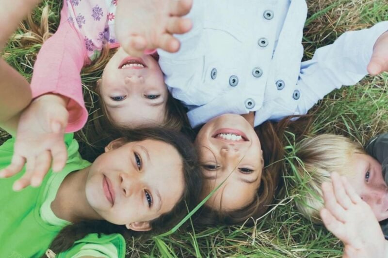 Niños sonrientes tumbados sobre la hierba – imagen que transmite felicidad, unión y bienestar.