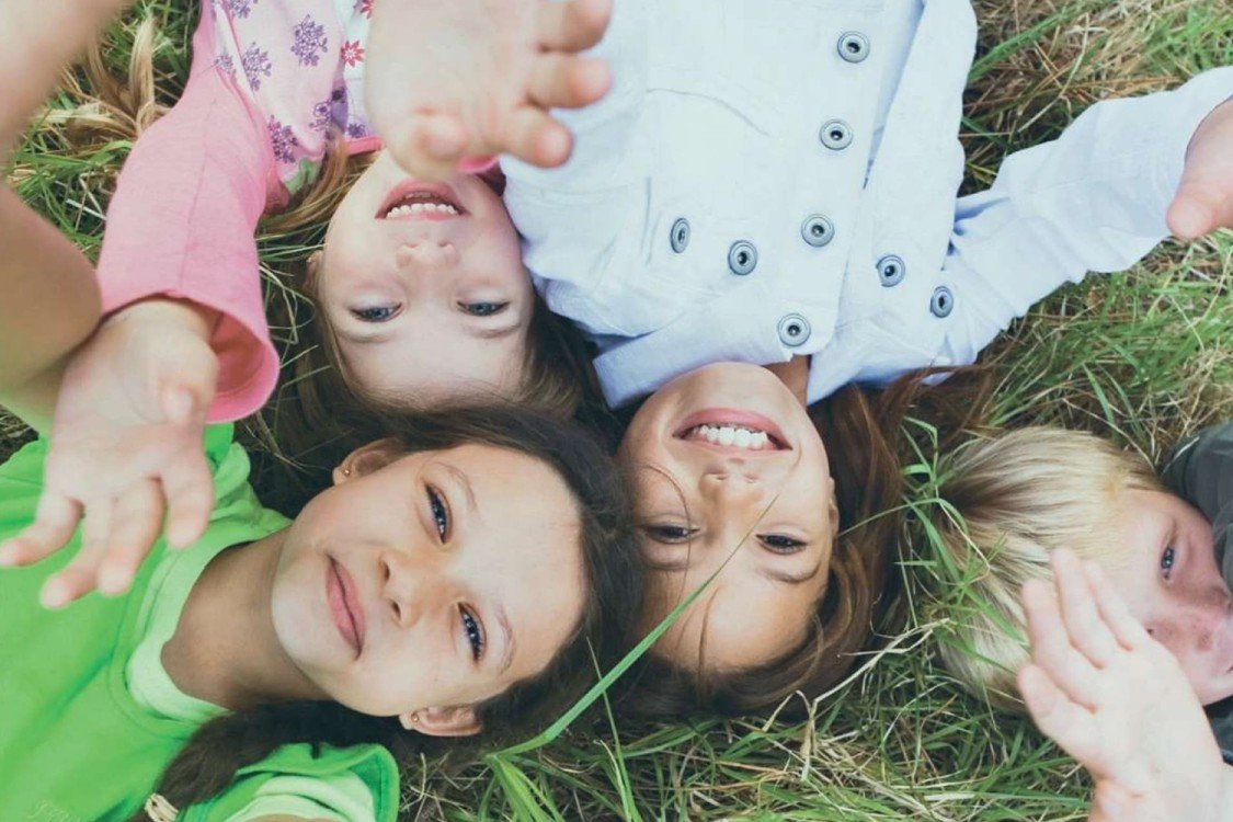 Niños sonrientes tumbados sobre la hierba – imagen que transmite felicidad, unión y bienestar.