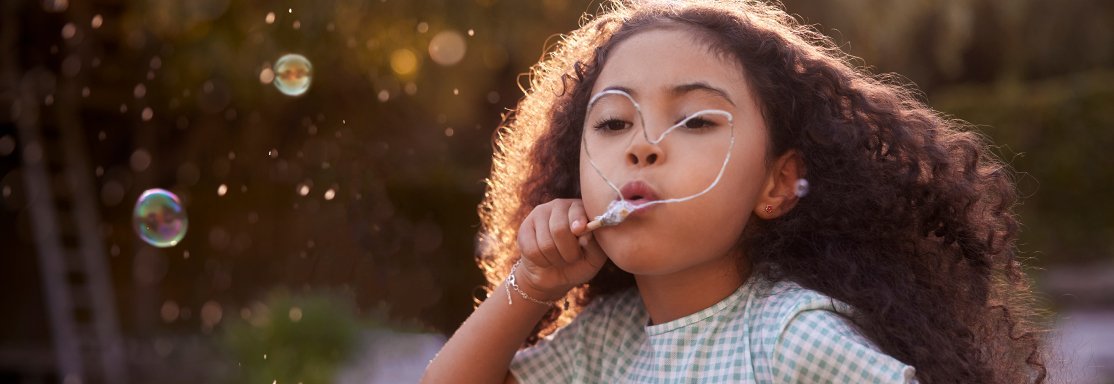 Niña soplando burbujas de jabón al aire libre, imagen poética y esperanzadora.