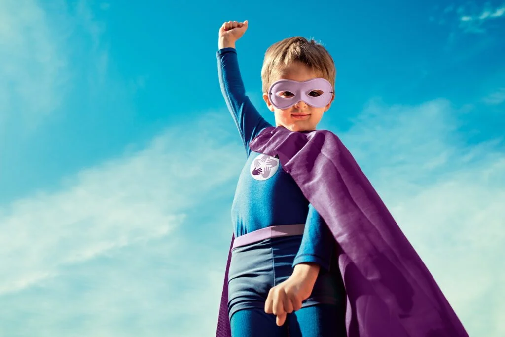 Niño disfrazado de superhéroe levantando el puño hacia el cielo, símbolo de fuerza y esperanza.